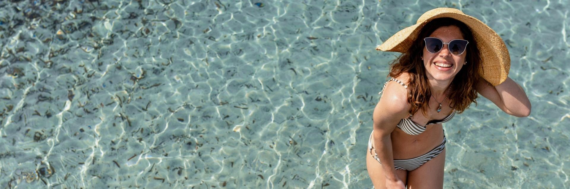 mujer con gafas de sol y sombrero en una playa de aguas cristalinas