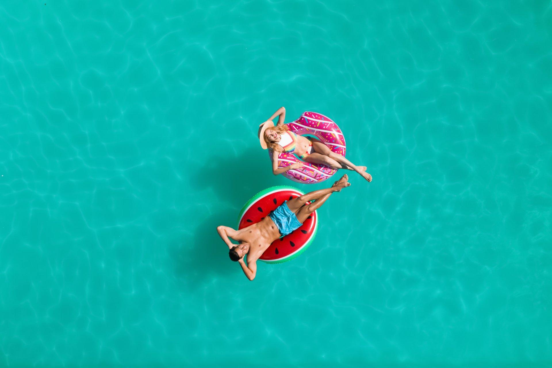 vista aérea de una pareja bañándose en el caribe con flotadores de colores